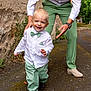 Noé a rejoint le concours — aidez-le/la à gagner de superbes lots ! toddler, child, adult, outdoor, smiling, walking, green_pants, white_shirt, bow_tie, supporting_hands, pathway, wall, plants, footwear, happy, person, nature, casual, family, daylight
