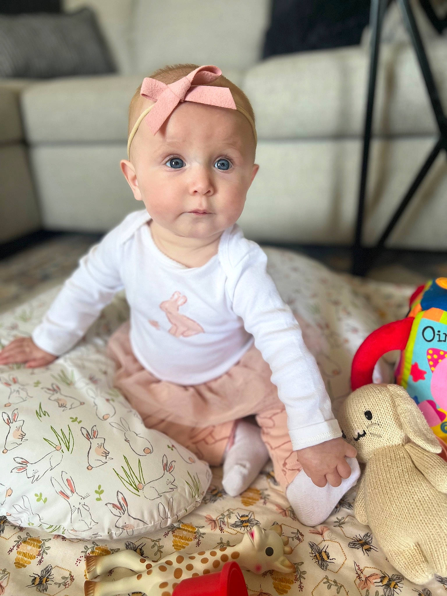 Katie is registered to the contest to win money with this photo: baby, baby_toddler_clothing, cheek, child, comfort, facial_expression, flooring, happy, linens, pattern, person, pink, sitting, skin, sleeve, surprise, t_shirt, textile, toddler, toy