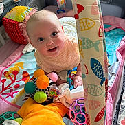 Grace is registered to the contest to win money with this photo: baby, child, playpen, toy, colorful, smiling, blanket, plush, face, infant, cute, happy, indoors, fabric, pattern, seating, soft, playtime, person, comfort
