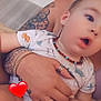 Melyo participe au concours pour gagner de l'argent avec cette photo : baby, child, person, tattoo, bracelet, necklace, hand, onesie, patterned_clothing, heart_emoji, adult, holding, curious_expression, indoor, couch, skin, jewelry, closeup, portrait, casual