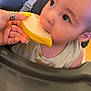 Melyo a rejoint le concours — aidez-le/la à gagner de superbes lots ! baby, child, high_chair, fruit, hand, nail_polish, yellow, bite, curious, messy, food, feeding, closeup, indoor, person, face, eyes, skin, clothing, seat