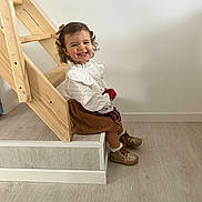Ava participe au concours pour gagner de l'argent avec cette photo : child, toddler, smile, curly_hair, bow, white_blouse, brown_skirt, shoes, stairs, wood, floor, indoor, happy, sitting, person, cute, young_child, portrait, home, casual