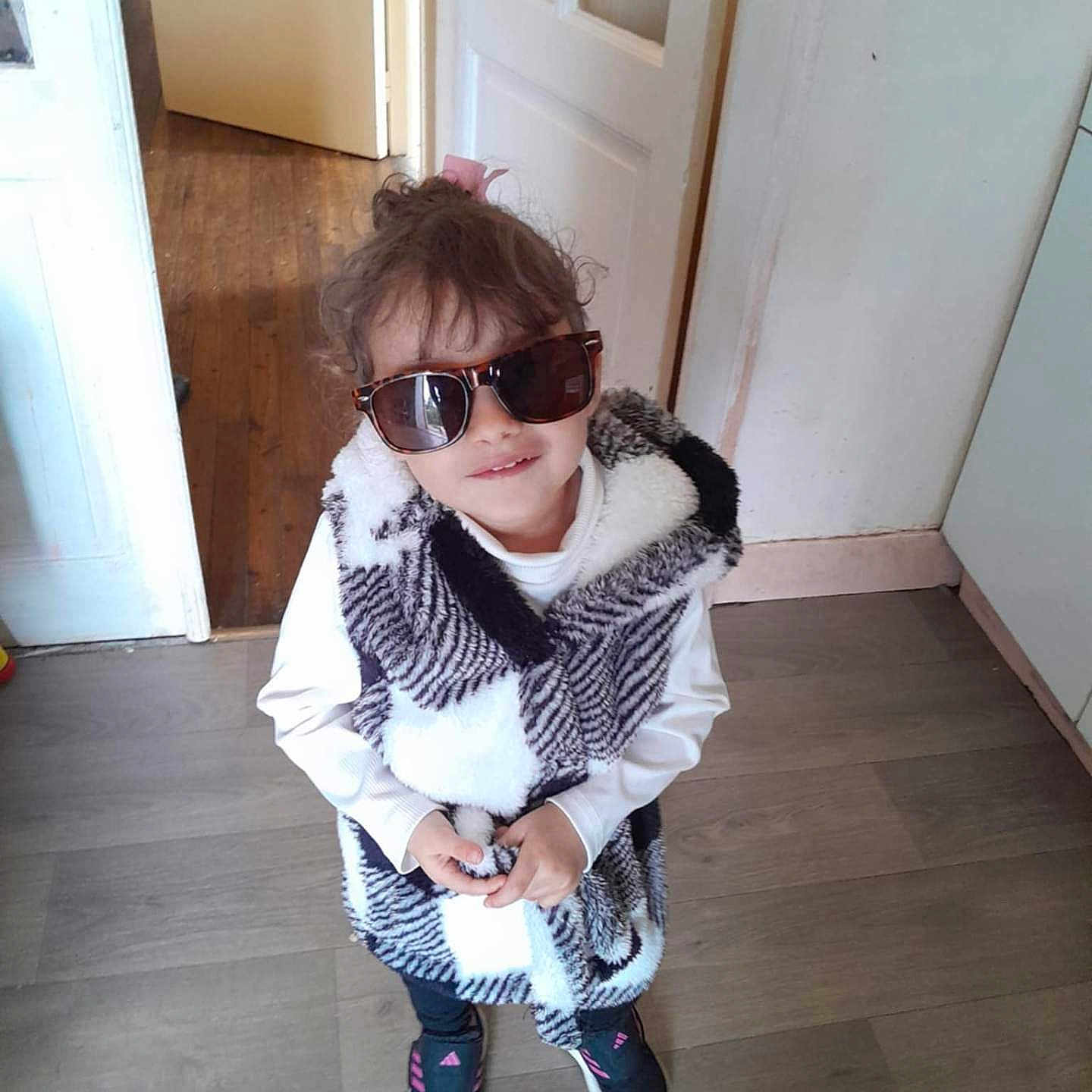 Mallaury participe au concours pour gagner de l'argent avec cette photo : black_pants, casual_clothing, child, cool, curly_hair, cute, door, fashion, footwear, home, indoor, person, pink_hair_tie, smile, sneakers, standing, sunglasses, vest, white_shirt, wooden_floor