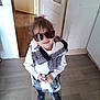 Mallaury a rejoint le concours — aidez-le/la à gagner de superbes lots ! black_pants, casual_clothing, child, cool, curly_hair, cute, door, fashion, footwear, home, indoor, person, pink_hair_tie, smile, sneakers, standing, sunglasses, vest, white_shirt, wooden_floor