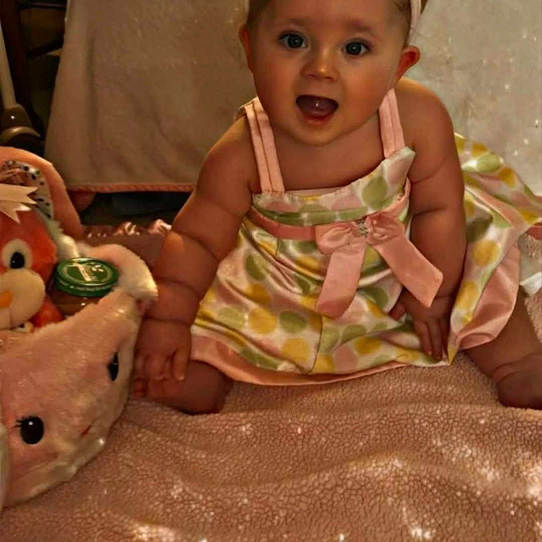 Rosavina is registered to the contest to win money with this photo: accessories, baby, bonnet, clothing, costume, couch, dress, face, formalwear, furniture, happy, hat, head, indoors, jewelry, person, photography, portrait, sitting, toy