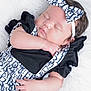 baby, sleeping, infant, headband, bow, black_clothing, white_background, soft_texture, peaceful, cute, portrait, child, closeup, newborn, hand, face, resting, adorable, fashion, soft_lighting