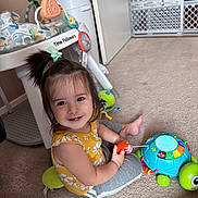 Leah joined the competition — help win amazing prizes! toddler, child, smiling, toy, carpet, indoor, yellow_clothing, gray_pants, hair_tie, colorful_toy, baby_activity_center, baby_gate, playtime, happy, cute, person, floor, home, childhood, infant