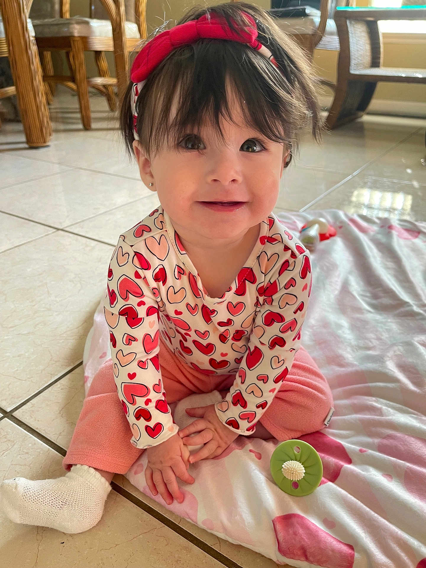 Leah joined the competition — help win amazing prizes! baby, toddler, child, smiling, sitting, headband, heart_pattern, pink_pants, onesie, blanket, toy, tile_floor, earrings, dark_hair, big_eyes, indoors, natural_light, portrait, cute, playtime