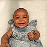 Milly is registered to the contest to win money with this photo: baby, smile, happy, infant, child, dress, floral_pattern, cute, portrait, lying_down, skin, face, hand, fingers, ruffle, fabric, joy, expression, indoors, soft_texture