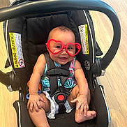 Milly joined the competition — help win amazing prizes! baby, heart_shaped_glasses, car_seat, smiling, child, infant, seatbelt, black_car_seat, happy, cute, indoor, wooden_floor, sitting, colorful_clothing, toddler, playful, adorable, young_child, glasses, seat