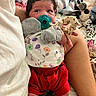 Isabella joined the competition — help win amazing prizes! baby, newborn, pacifier, infant, clothing, mittens, socks, person, bed, blanket, plush_toy, colorful, indoor, comfort, holding, curly_hair, red_shorts, floral_pattern, soft_lighting, resting