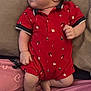 baby, infant, red_clothing, romper, candy_cane_pattern, gift_pattern, lying_down, curious_expression, soft_surface, pink_clothing, heart_pattern, hand, skin, face, foot, leg, person, child, indoors, casual