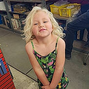 Freyja is registered to the contest to win money with this photo: child, blonde_hair, dress, shoes, workshop, garage, shelf, tools, floor, person, standing, smiling, curly_hair, concrete_floor, casual_clothing, indoor, yellow_basket, metal_shelves, playful, young_child
