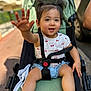 Mia participe au concours pour gagner de l'argent avec cette photo : toddler, child, stroller, outdoor, smiling, pigtails, shorts, shirt, sandals, hand, seatbelt, sunlight, happy, baby, person, casual_clothing, daylight, urban, cute, playful