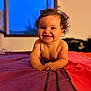 baby, child, smile, curly_hair, bed, indoor, window, evening, blue_sky, skin, portrait, happy, infant, lying_down, warm_lighting, room, colorful_bedspread, hands, face, cute