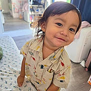 Franco is registered to the contest to win money with this photo: child, toddler, smiling, portrait, indoors, bedroom, bed, bedspread, clothing, shirt, fish_pattern, dark_hair, brown_eyes, sitting, leaning, camera, wardrobe, window, home, happy