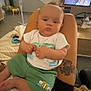 baby, blanket, bottle, casual, child, clothing, face, fan, floor, furniture, human, indoor, legs, living_room, person, shorts, sitting, tattoo, television, tshirt