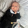 baby, infant, black_dress, white_collar, blanket, plush, beads, pacifier_clip, face, head, person, cute, lying_down, soft_texture, indoors, newborn, expression, clothing, accessory, resting