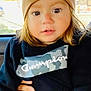 toddler, child, beanie, hoodie, clothing, face, person, sitting, indoors, hand, car_interior, expression, cute, young_child, casual_wear, portrait, brown_hair, long_hair, fashion, warm_clothing