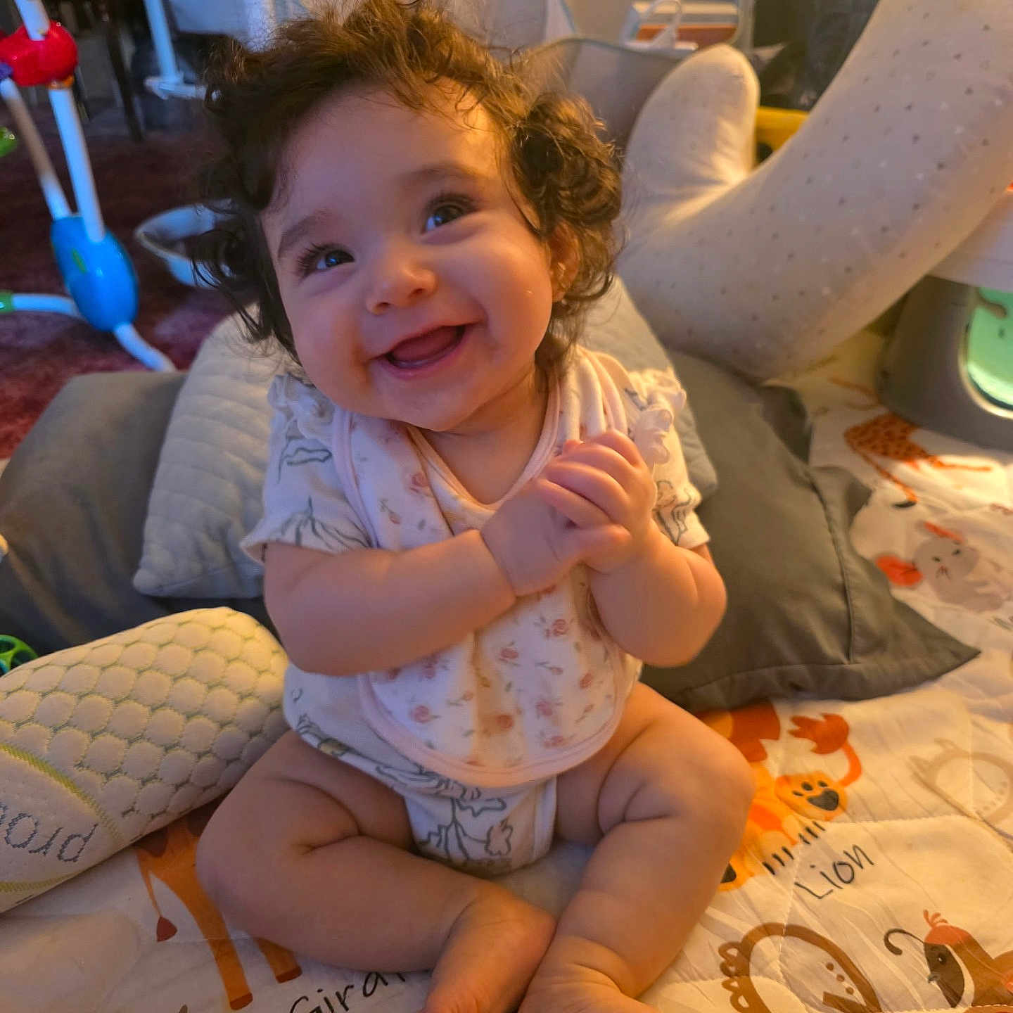 Jessie is registered to the contest to win money with this photo: baby, child, toddler, smiling, happy, curly_hair, portrait, sitting, indoors, playroom, play_mat, infant, baby_clothing, bare_feet, toys, cushion, furniture, warm_lighting, family_home, cute