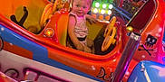 Grâce participe au concours pour gagner de l'argent avec cette photo : amusement_park, amusement_ride, backpack, blonde_hair, bright_colors, carnival, child, colorful_lights, entertainment, family_fun, fun, indoor, person, playful, ride, seat, smiling, toddler, toy_car, young_child