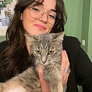Hoshi participe au concours pour gagner de l'argent avec cette photo : woman, cat, glasses, smile, indoor, pet, holding, gray_cat, long_hair, jewelry, bracelet, ring, green_wall, portrait, casual, happy, feline, household, cute, cozy