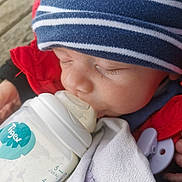 Gaetan a rejoint le concours — aidez-le/la à gagner de superbes lots ! baby, infant, sleeping, bottle, feeding, beanie, striped_hat, eyelashes, milk_bottle, pacifier_clip, blanket, red_jacket, close_up, face, newborn, hand, outdoor, wooden_deck, nap, peaceful
