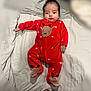baby, infant, red_onesie, reindeer_pattern, footed_pajamas, blanket, lying_down, indoor, cute, child, portrait, newborn, cozy, soft_fabric, clothing, person, face, hair, expression, holiday_theme