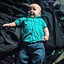 baby, blanket, blue_jeans, casual_clothing, child, curious_expression, face, footwear_absent, head, indoor, infant, lying_down, natural_light, person, relaxed_pose, skin, small_hands, soft_fabric, turquoise_shirt, young_child