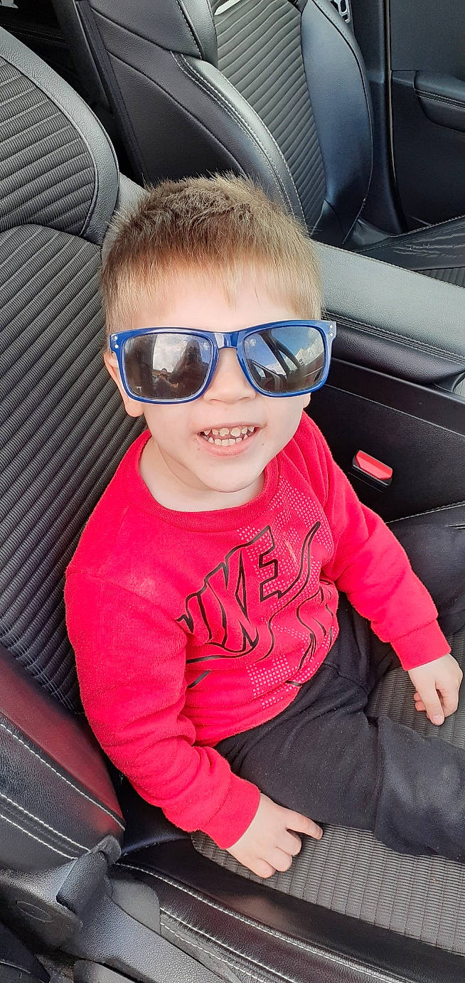 Elliott participe au concours pour gagner de l'argent avec cette photo : auto_part, automotive_design, automotive_exterior, bumper, car_seat, comfort, cool, eyewear, glasses, goggles, lip, motor_vehicle, mouth, person, smile, sunglasses, tints_and_shades, toddler, vehicle_door, vision_care