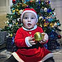baby, child, christmas_tree, ornament, holiday, festive, red_clothing, santa_hat, indoor, decorations, presents, sparkle, glitter, cute, celebration, seasonal, smiling, sitting, person, toy