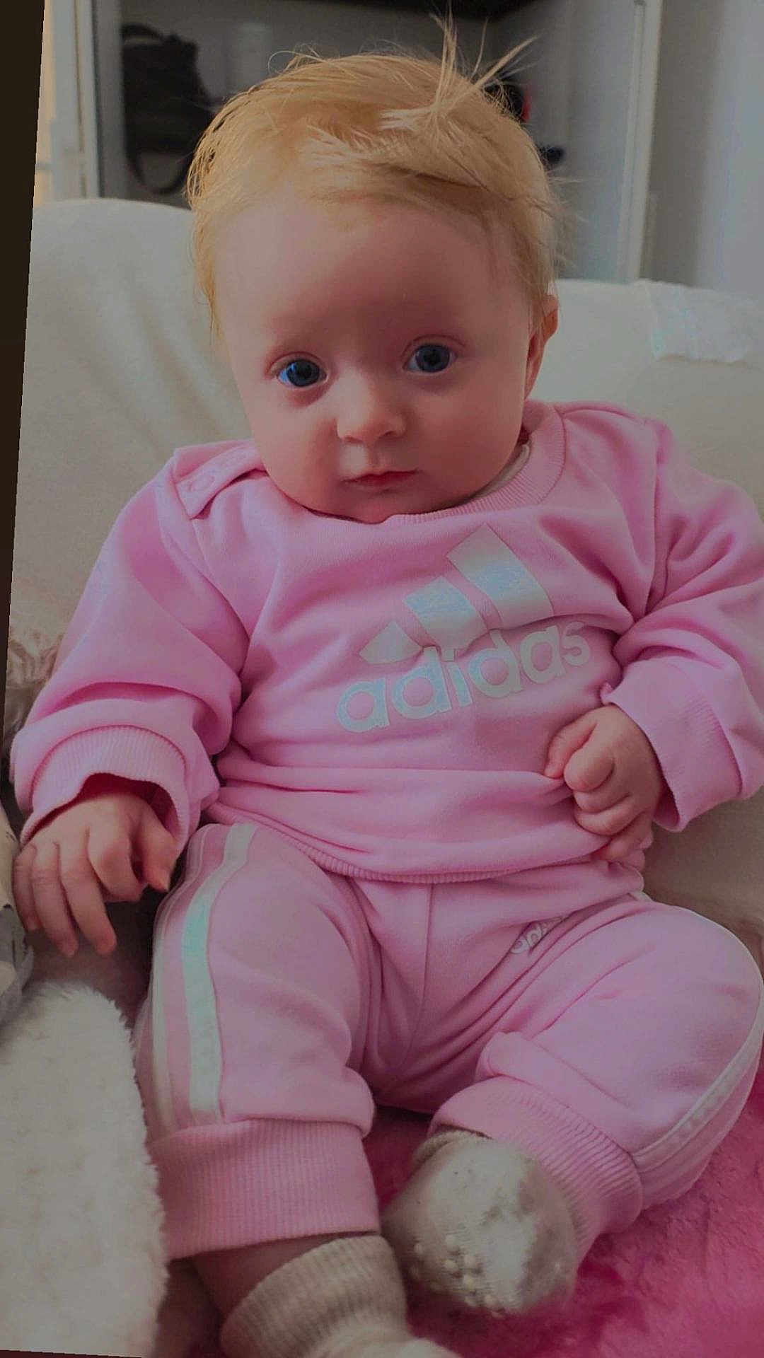 Selena participe au concours pour gagner de l'argent avec cette photo : baby, infant, child, pink_clothing, tracksuit, adidas, sitting, indoor, portrait, blue_eyes, blonde_hair, cozy, cute, soft_lighting, sock, casual_wear, hand, face, young_child, comfort