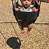 baby, child, swing, playground, wood_chips, hoodie, headband, yellow, brown, red, grass, sunlight, shadow, outdoor, infant, seat, toy, fun, park, person