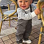 Meylan participe au concours pour gagner de l'argent avec cette photo : toddler, child, smiling, standing, striped_clothing, overalls, white_sneakers, wicker_chair, outdoor, cafe, brick_floor, happy, blue_eyes, short_hair, person, daylight, casual_wear, cute, playful, holding