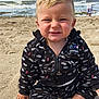 child, toddler, beach, sand, ocean, waves, smile, black_clothing, bmw_motorsport, sitting, happy, blond_hair, blue_eyes, casual_wear, outdoor, daylight, person, water, nature, playful