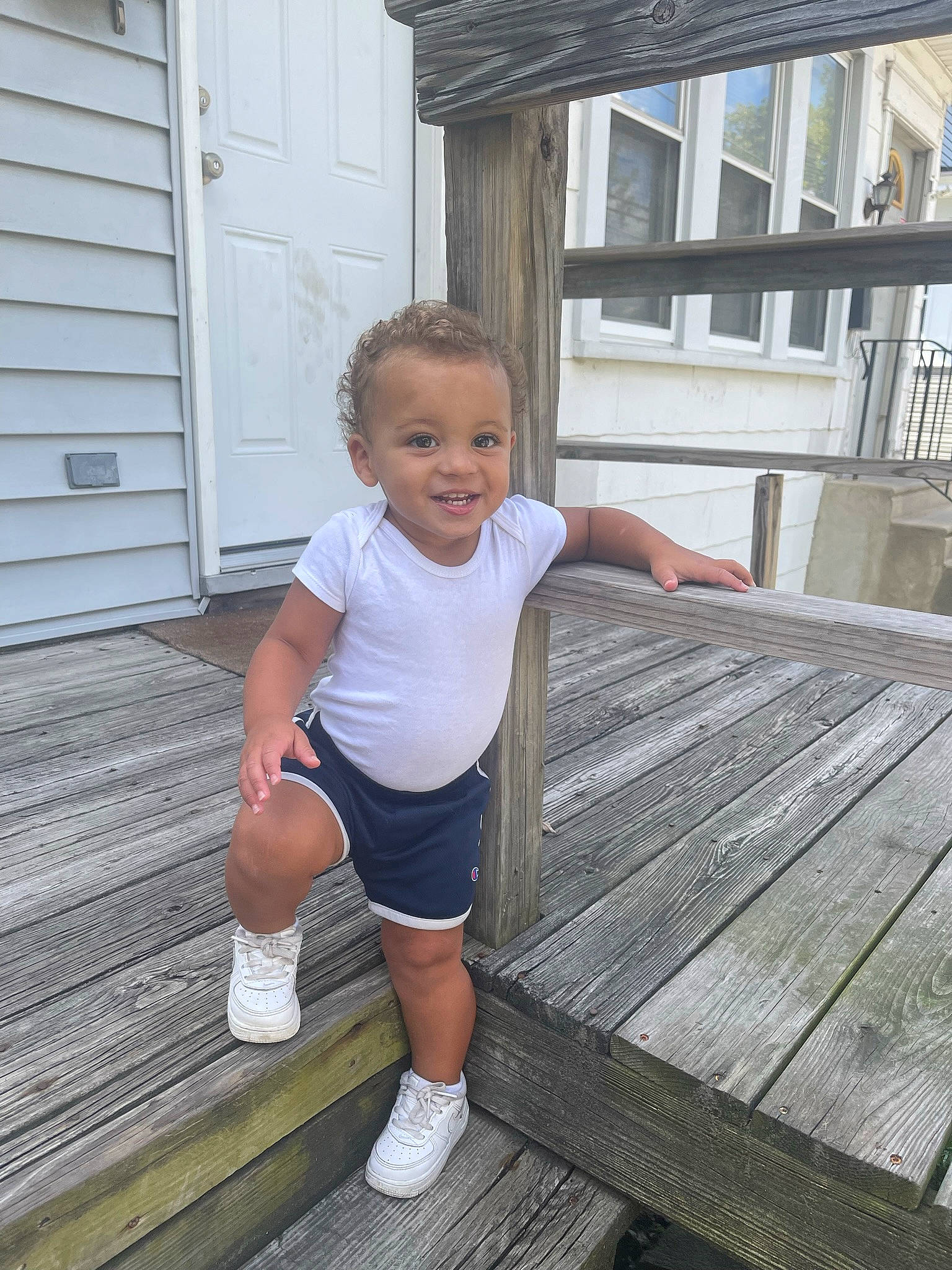 Angelo is registered to the contest to win money with this photo: composite_material, deck, door, flooring, grass, happy, hardwood, house, human_leg, joy, knee, leg, leisure, person, plank, shorts, smile, t_shirt, thigh, toddler