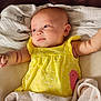 baby, infant, newborn, child, face, eyes, arm, hand, yellow_dress, polka_dot, blanket, swaddle, cloth, leather_sofa, zebra_print, portrait, indoor, soft_lighting, cute, smile