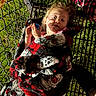 child, blanket, patterned_blanket, metal_grate, grass, outdoor, night, lighting, shadow, person, face, hand, red, black, white, pink, toy, fence, warm, cozy