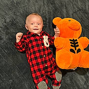Kage is registered to the contest to win money with this photo: baby, infant, smiling, red_checkered_onesie, plush_toy, orange_teddy_bear, soft_blanket, lying_down, cute, child, happy, cozy, indoor, small_hands, socks, playful, toy, fabric, portrait, young