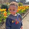 Isaac participe au concours pour gagner de l'argent avec cette photo : toddler, child, curly_hair, sweatshirt, colorful_text, outdoor, flower_bed, tulips, sunlight, side_view, pathway, spring, casual_clothing, young_kid, nature, daylight, portrait, cute, garden, plants