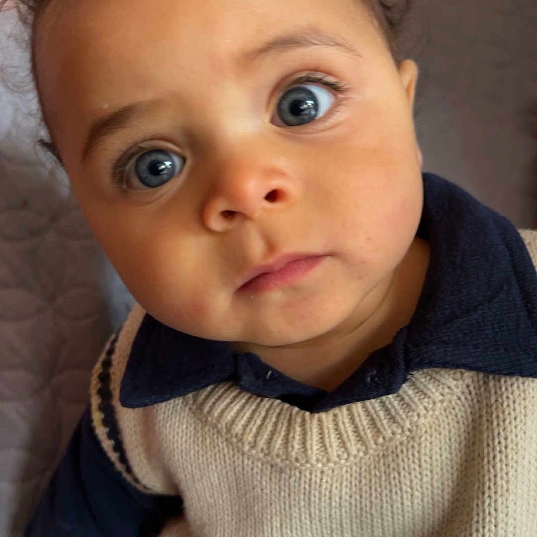 Isaac a rejoint le concours — aidez-le/la à gagner de superbes lots ! toddler, child, face, eyes, curly_hair, knit_vest, sweater, blue_shirt, denim, hand, portrait, indoor, baby, closeup, cute, person, seated, expression, soft_lighting, curious