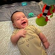 Ryker Zuniga is registered to the contest to win money with this photo: baby, infant, smile, onesie, toy, blanket, pattern, lying_down, happy, cute, child, playful, indoors, face, hand, clothing, pacifier, fabric, colorful, doll