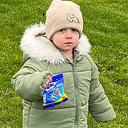 Noah is registered to the contest to win money with this photo: baby, cap, clothing, coat, face, glove, grass, hat, head, hood, hoodie, jacket, knitwear, lawn, person, photography, plant, portrait, sweater, sweatshirt