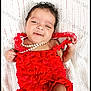 baby, infant, red_dress, pearl_necklace, smile, sleepy, curly_hair, blanket, white_background, portrait, cute, child, lying_down, indoors, soft_lighting, adorable, small_hands, fashion, newborn, happy
