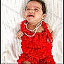 baby, infant, red_clothing, pearls, knitted_blanket, cute, portrait, child, smiling, lying_down, indoors, young, adorable, fashion, accessory, happy, skin, hair, expression, closeup