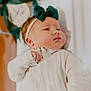 baby, infant, headband, bow, white_onesie, sleepwear, face, skin, cheeks, hand, newborn, lying_down, indoors, soft_lighting, blurred_background, peaceful, cute, child, portrait, toddler
