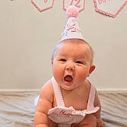 Blakely is registered to the contest to win money with this photo: adorable, baby, banner, birthday, blanket, celebration, child, cute, event, expression, half_birthday, headwear, indoors, infant, party_hat, person, pink, sitting, smile, young_child