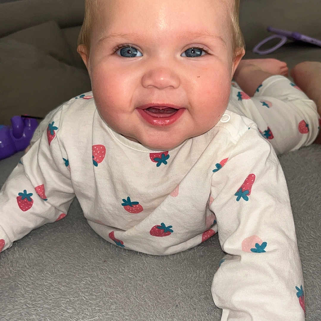 Ambre participe au concours pour gagner de l'argent avec cette photo : baby, blue_eyes, cheeks, child, closeup, clothing, crawling, cute, face, hand, happy, indoor, infant, long_sleeve, person, portrait, skin, smiling, soft_surface, strawberry_pattern