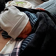 Hermes is registered to the contest to win money with this photo: baby, newborn, infant, sleeping, beanie, blanket, striped_clothing, swaddle, adult_chest, necklace, hand, indoor, cozy, lounger, pajamas, closeup, portrait, soft_fabric, wood_floor, nursery_accessory