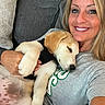 woman, puppy, dog, smiling, sleeping, couch, indoor, casual, light_hair, tshirt, pet, happy, closeup, relaxed, affection, holding, comfortable, resting, face, human